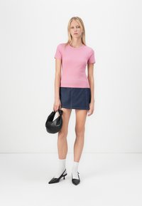 Rosa ribbet kortermet topp, denim miniskjørt med kontrastsømmer, svart håndveske, hvite sokker og spisse svarte hæler.