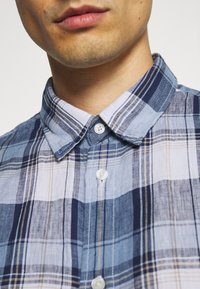 Blå och vit rutig skjorta med krage, med ljusa och mörka blå rutor, gula accenter och vita knappar.