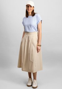 Light blue short-sleeve t-shirt, beige pleated midi skirt, and white sneakers with a textured sole. beige cap with subtle logo detail.