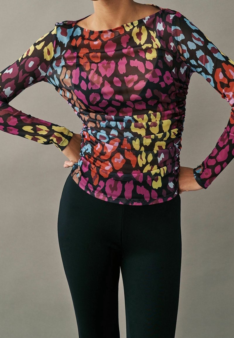 Personne portant un haut ajusté à manches longues avec un imprimé animalier coloré en rouge, jaune, bleu et violet, associé à un pantalon noir uni.