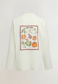 White long-sleeve shirt with a colorful vegetable illustration and "Family Recipe" text framed in red on the back.