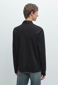 Schwarzes Langarmhemd mit Kragen, das eine glatte Textur, eine lockere Passform und ein minimalistisches Design aufweist, kombiniert mit hellblauen Jeans.