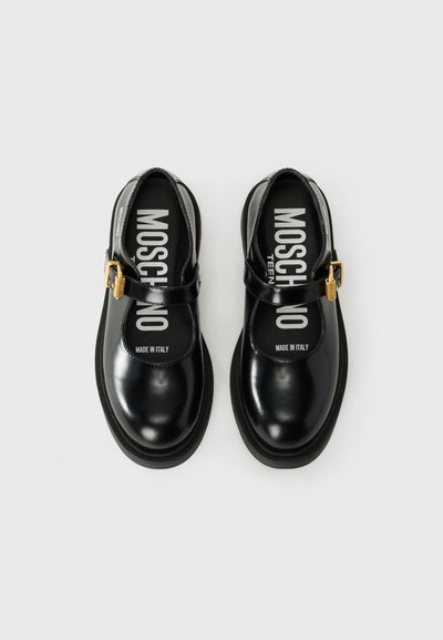 Svarta lackläderskor med rund tå, ankelrem och guldaccenter. "MOSCHINO TEEN" tryckt på innersulorna. Platt gummisula.