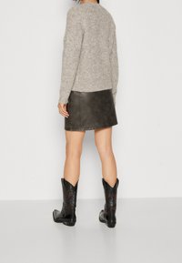 Szary sweter dzianinowy, czarna skórzana spódnica mini i czarne kowbojskie botki z misternymi wzorami. Osoba pokazana od tyłu.