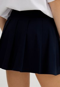 Falda plisada azul marino hecha de un tejido ligero, que cuenta con una cinturilla que se sitúa justo por encima de las caderas y una textura suave.