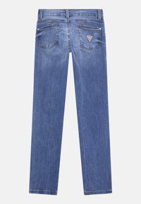 Jean en denim, bleu clair, coupe droite, avec deux poches arrière et un patch logo en forme de triangle sur la poche droite.