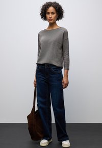 Grijze langemouwen top met een gestructureerd patroon, gecombineerd met donkerblauwe wijde jeans en witte sneakers, met een bruine suède tote bag.