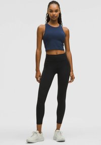 Navy cropped athletic tank top with a high neckline, paired with black high-waisted leggings and white sneakers. Smooth texture, fitted design.