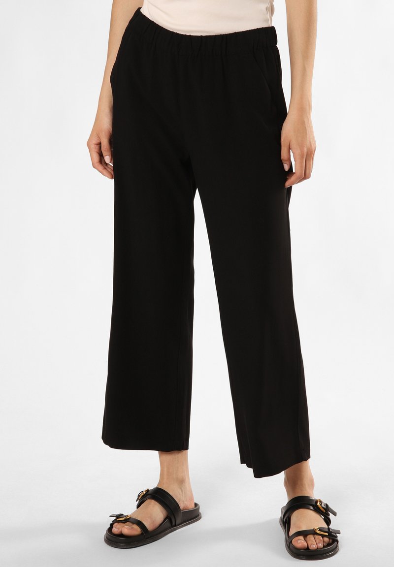 Schwarze, weit geschnittene Hose mit elastischem Bund, aus einem glatten Stoff gefertigt. Kombiniert mit schwarzen Sandalen mit dekorativem Schnallendetail.