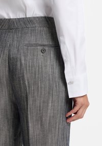 Szürke csíkos nadrág, szabott fazonú, hátul gombbal záródó zsebbel, valamint egy sima fehér ing mandzsetta részletekkel.