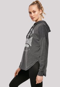Grå hettegenser med stort hvitt grafisk trykk, snorhett, lange ermer og splitt i siden, sammen med svarte leggings.
