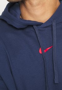Navy blue hoodie made of soft fabric, featuring a kangaroo pocket, drawstring hood, and a red Nike logo on the chest.