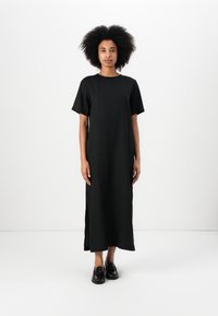 Black, short-sleeve, maxi dress made of soft fabric with side slits. Features a round neck and a loose-fitting design. Worn with black shoes.