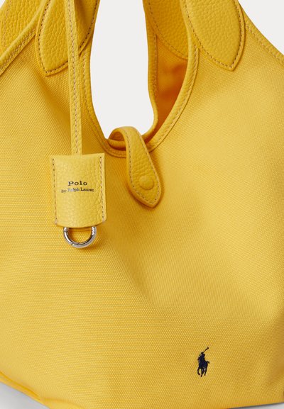 Gul stof- og lædertaske med syet håndtag, knappet remslynge, metalring og lille broderet mørkeblå hestelogo.