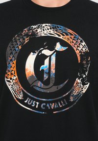 Mustapaita, jossa on värikäs pyöreä käärme -kuvio, joka ympäröi tyyliteltyä "J"-kirjainta ja "Just Cavalli" -tekstiä alaosassa keskellä.