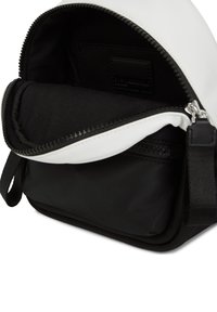 Borsa con cerniera in bianco e nero con parte superiore arrotondata, dotata di un ampio interno in tessuto nero e di una tasca con zip sul lato.
