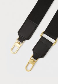 Musta kudottu hihna, jossa on kultasävyinen metalliosat, nahkaosuudet ja klipsikiinnikkeet varmasta kiinnityksestä.