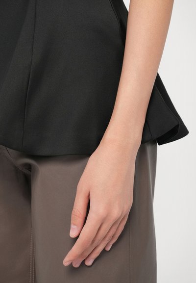 Top negru structurat cu un tiv evazat, asortat cu pantaloni maroon netezi. Prim-plan al unei mâini odihnindu-se pe zona coapsei pantalonilor.