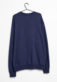 Mörkblå tröja med långa ärmar, ribbade manchetter och nederkant. Bakom finns en rektangulär patch och en jämn textur. Den hänger fr ån en svart krok.