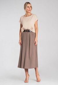 Beżowa teksturowana bluzka połączona z brązową plisowaną spódnicą midi, zaciśnięta szerokim brązowym paskiem. Przezroczyste sandały na obcasie dopełniają ten look.