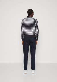 Un pull rayé bleu marine et blanc avec un col rond, des poignets et un ourlet côtelés ; associé à un pantalon bleu marine et des chaussures de sport blanches.