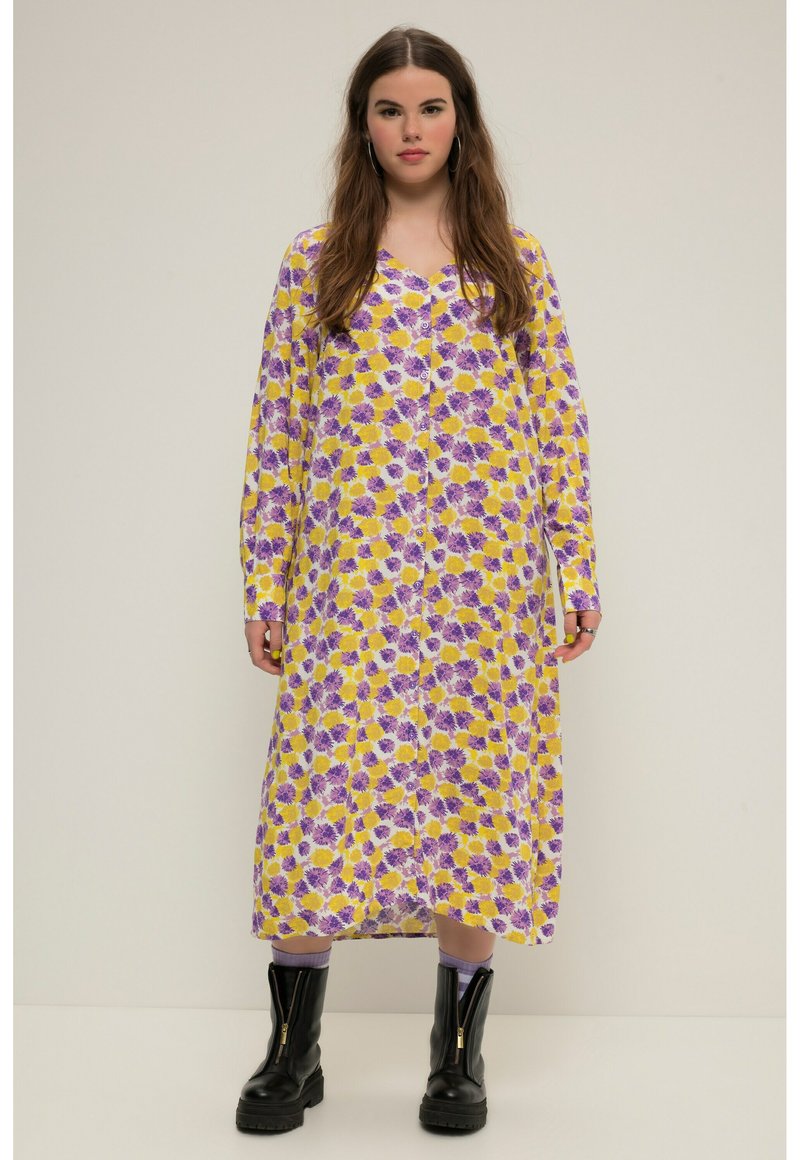 Vestido largo con estampado floral amarillo y púrpura, con botones en el frente, mangas largas y un corte holgado, combinado con botas negras gruesas.