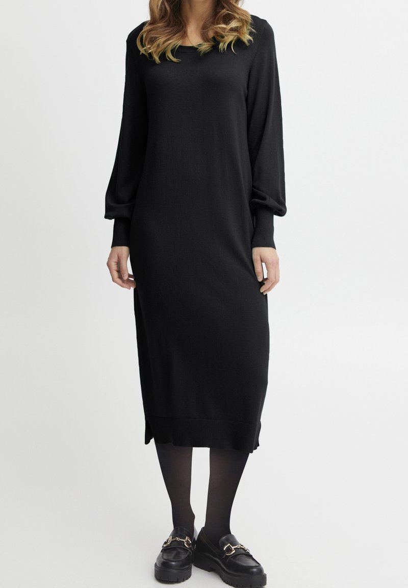 Svart stickad klänning med långa, puffärmar, en rundad halsringning och slitsar i sidan vid fållen. Matchas med svarta plattformsskor.