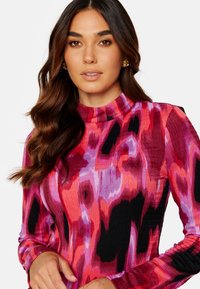 Langdurige jurk in een levendig roze en paarse abstracte patroon met ribbeltextuur. Hoog halsontwerp en contrasterende zwarte accenten langs de mouwen.