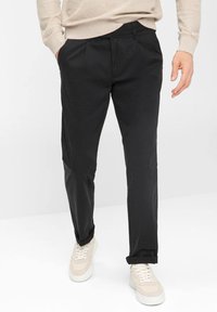 Pantaloni neri con vestibilità slim, realizzati in tessuto leggero, dotati di pieghe frontali e tasche laterali, abbinati a sneaker di colore chiaro.