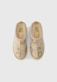 Μπεζ σουέντ παντόφλες με κεντήματα λουλουδιών, ροζ διακοσμητική ραφή και μαλακή επένδυση από λευκή κρεμ shearling, απεικονιζόμενες από ψηλά.