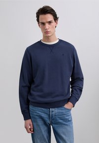 Mørkeblå sweatshirt med rund hals, ribbede manchetter og kant. Har en subtil korsstingdetalje og et lille logo på brystet.