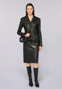 Schwarze Leder-Blazer mit einem Reverskragen, kombiniert mit einem eng anliegenden schwarzen Lederrock und kniehohen schwarzen Stiefeln, die eine schlanke Silhouette schaffen.