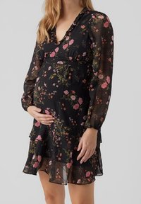 Raskausmekko mustasta läpinäkyvästä kankaasta, jossa on monivärinen kukkakuosi, syvä v-pääntie, pitkät puffihihat ja kerroksellinen röyhelöhelma.