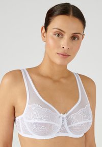 Soutien-gorge en dentelle blanche avec un haut en mesh, des bonnets moulés et des coutures décoratives le long de l'encolure, agrémenté d'un petit nœud au centre.