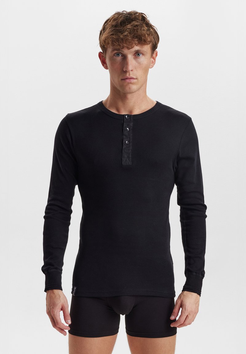 Svart langermet skjorte laget av mykt stoff, med rund hals, fire knappelukking og tettsittende design. Synlig logo på kanten.