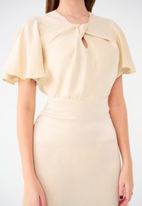 Beiges Kleid mit kurzen schwingenden Ärmeln, einem Schlüsselloch-Detail am Ausschnitt und einer taillierten Passform. Glatte Textur und leichtes Material.