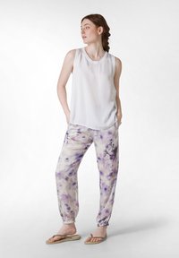 Vit ärmlös topp och lösa byxor i ljuslila med blommönster. Byxorna har elastiska muddar, mjukt tyg och är kombinerade med flip-flops.