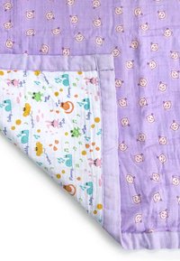 Baby blanket with purple border and smiling baby face pattern, folded to reveal white underside with colorful animal and nature prints.