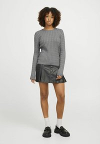 Maglione grigio a coste con maniche lunghe. Abbinato a una gonna svasata nera in pelle sintetica. Scarpe con piattaforma nere e calzini bianchi.