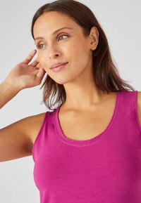 Top de tirantes fucsia con escote redondeado, borde ondulado y tejido suave y ligero; textura lisa, diseño informal.