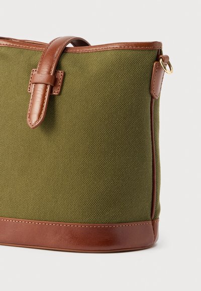 Πράσινη υφασμάτινη τσάντα ώμου με καφέ λεπτομέρειες από δέρμα, λουρί και μικρό χρυσό μεταλλικό δαχτυλίδι στο πλάι.