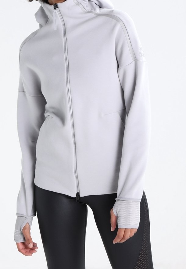 Chaqueta de punto gris claro con capucha, con detalles de mangas acanaladas y costuras planas, combinada con leggings negros ajustados.