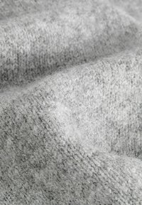 Tissu en laine tricoté doux et gris clair avec une surface texturée et duveteuse et des motifs de points visibles, montré en gros plan.