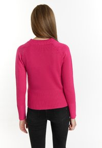 Maglione rosa aderente con bordo e polsini a coste, tessuto a maglia testurizzato e maniche raglan. La vista posteriore mostra un design semplice e pulito.