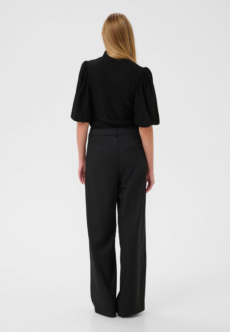 Top negro de manga abullonada con un cuerpo ajustado, combinado con pantalones anchos negros que tienen un bolsillo trasero y una cinturilla sin costuras.