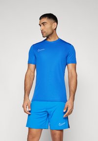 Blå Nike treningsskjorte og shorts. Laget av lett stoff. Har rund hals, korte ermer og hvite Nike-logo detaljer.