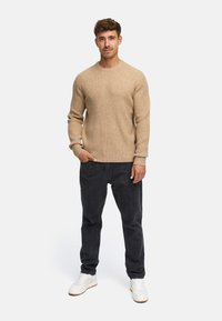 Maglione a coste beige con collo rotondo, abbinato a jeans scuri e Sneakers bianche. Presenta un look casual e aderente.