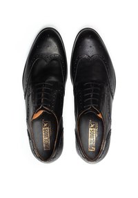 Scarpe brogue in pelle nera con dettagli perforati, punta tonda e allacciatura tradizionale. Texture liscia con accenti di cucitura discreti.