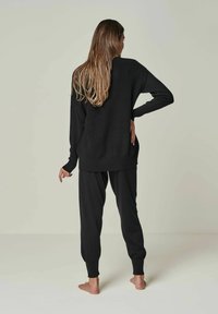Black knit sweater and matching joggers, loose-fitting with long sleeves and cuffed ankles, soft texture, worn barefoot.