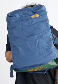 Blue backpack with green accents, made of durable fabric, featuring a logo on the front, padded straps, and multiple compartments.